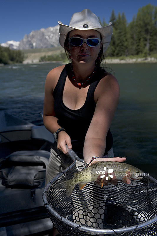 戴牛仔帽的年轻女人手持渔网展示割喉鳟鱼图片素材