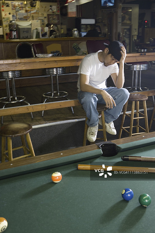 沮丧的男人穿着牛仔裤和T恤坐在台球桌旁图片素材