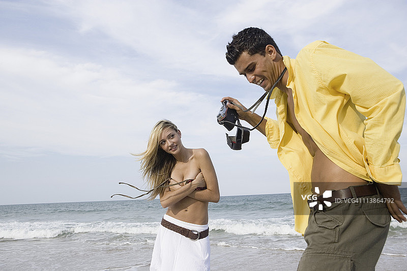 年轻男人在海滩上拍摄衣着暴露的女人图片素材