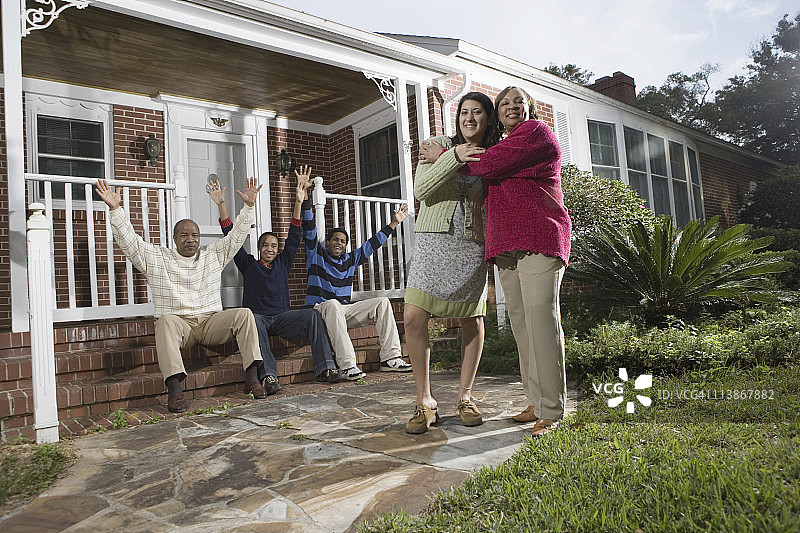 婆媳在房子前拥抱，家人在背景中图片素材