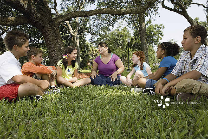 孩子们和老师在公园的草地上围成一圈图片素材