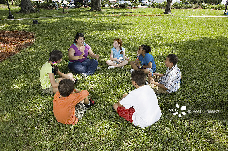 孩子们和老师在公园的草地上围成一圈图片素材