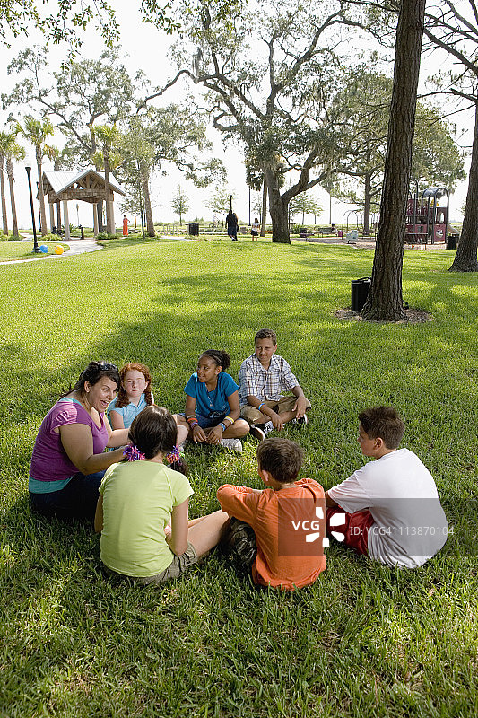 孩子们和老师在公园的草地上围成一圈图片素材