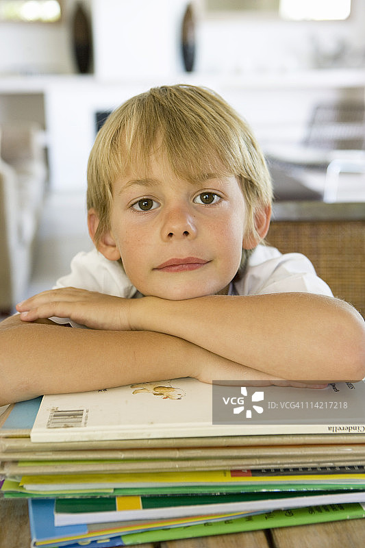 男孩靠在一堆书上，看起来很无聊，南非西开普省开普敦图片素材