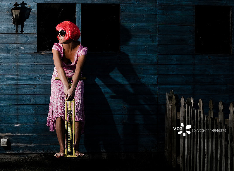 穿着晚礼服踩着弹簧单高跷站在小屋旁的女人图片素材