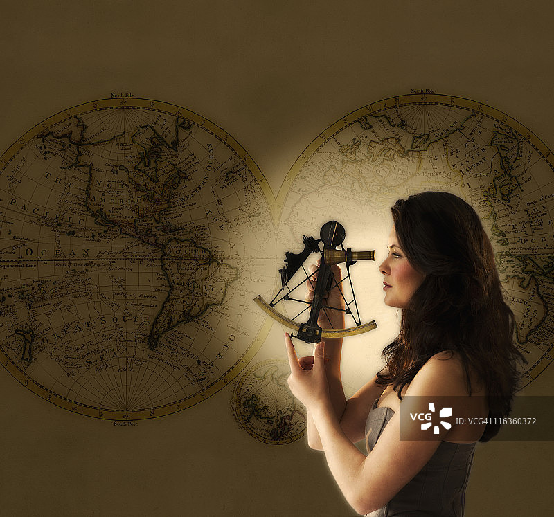 女人用古董六分仪观看，背景是世界地图图片素材