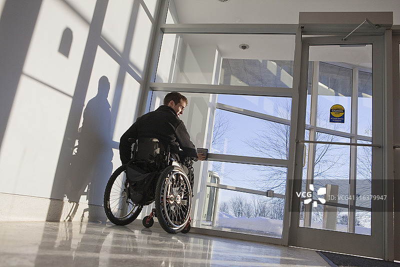 脊髓损伤男子乘坐轮椅按下按钮打开门图片素材