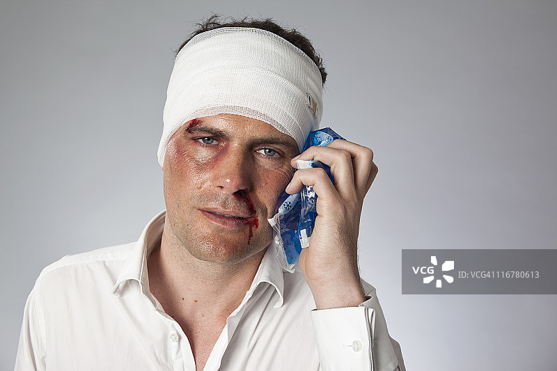 男子脸上有瘀伤，头部缠着绷带，用冰袋敷脸图片素材