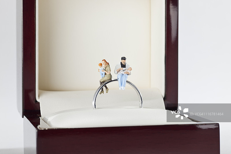 年轻家庭坐在珠宝盒结婚戒指上的微型雕像图片素材