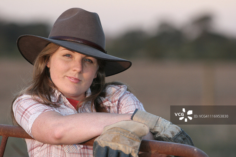 戴牛仔帽和手套，站在铁门旁的女人肖像图片素材