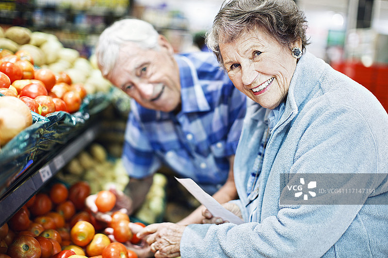 快乐的老年夫妇在超市挑选西红柿，面带微笑图片素材