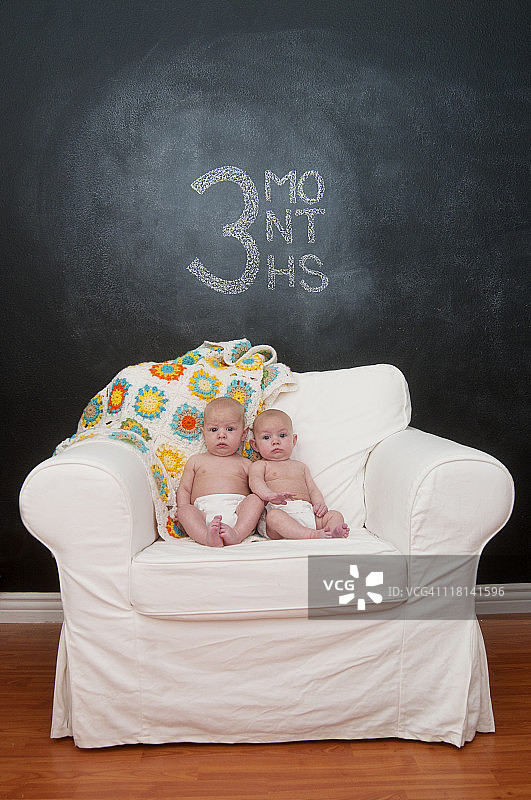 坐着拍摄每月成长照片的双胞胎婴儿图片素材