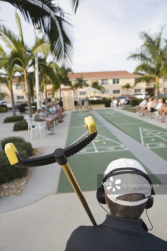 拿着沙狐球棒并戴着耳机的老年男人的背影图片素材