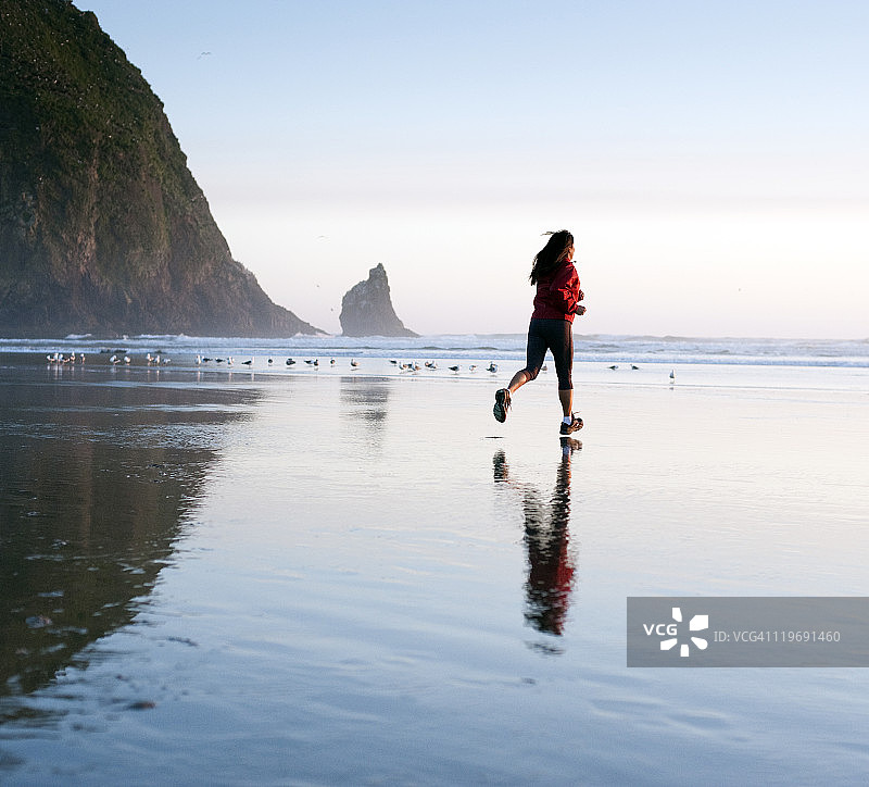 在干草堆岩附近海滩上慢跑的女人图片素材