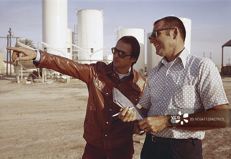 男人们指向前方，背景是储罐图片素材