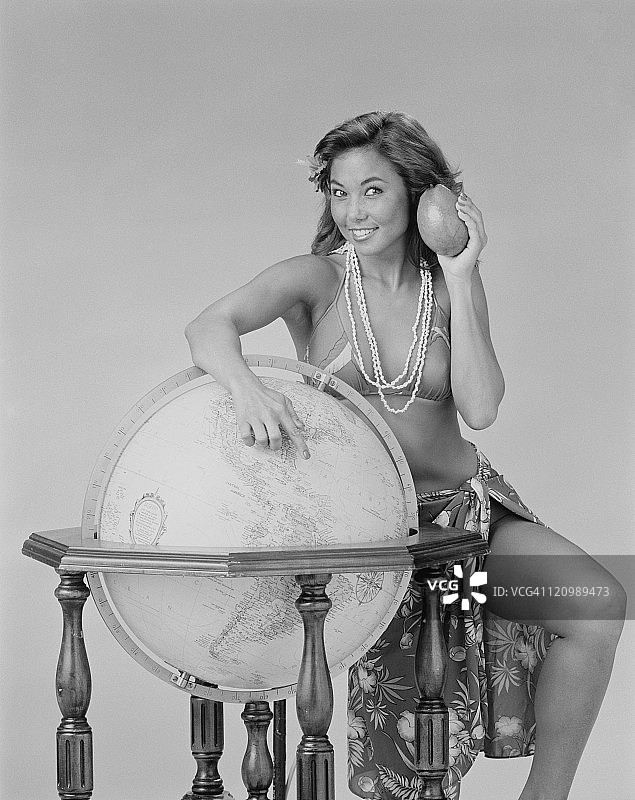 年轻女人手持牛油果站在地球仪旁，面带微笑图片素材