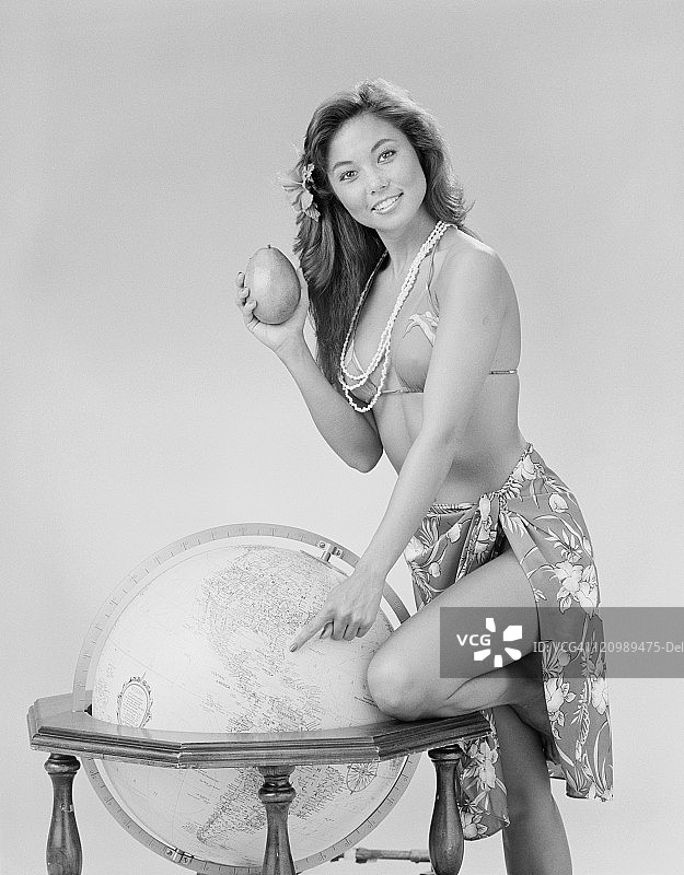 手持牛油果并指向地球仪的微笑年轻女人肖像图片素材