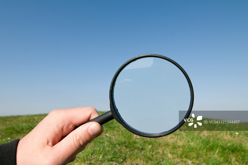 手持放大镜观察山丘和天空图片素材