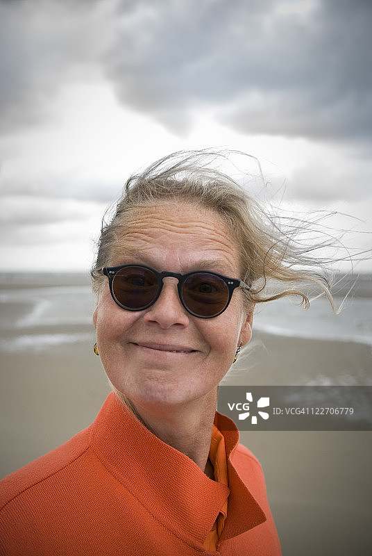 戴着太阳镜在海滩上开心微笑的50岁女人，留白图片素材