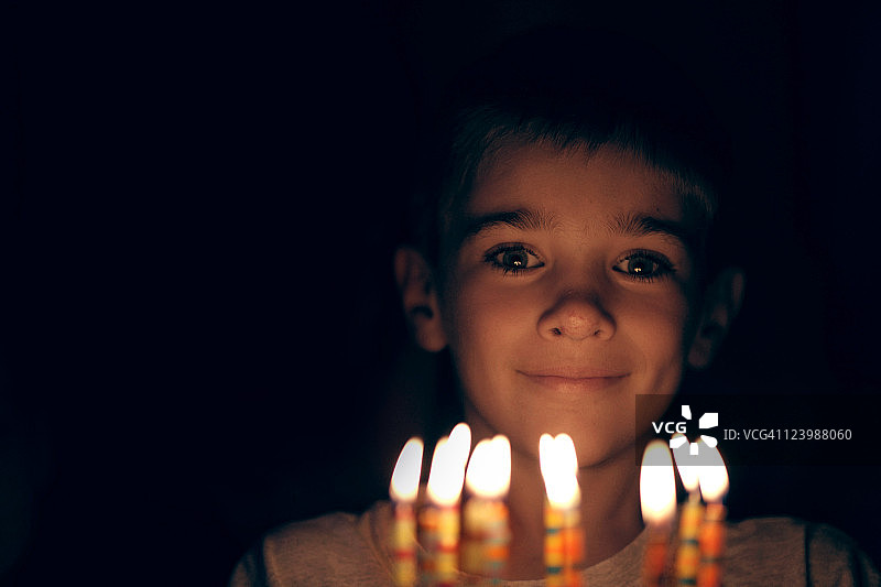 男孩面带微笑，看着生日蜡烛图片素材