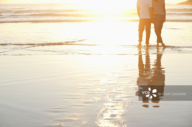 一对夫妇在日落时分站在海滩上的背影图片素材