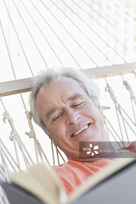 快乐的老年男人在吊床上看书特写图片素材