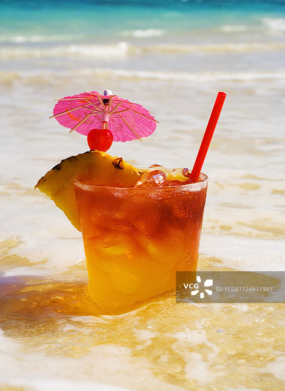 装饰有菠萝和樱桃的迈泰鸡尾酒，位于海滩的浅水中图片素材