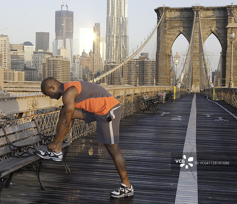 在布鲁克林大桥上系鞋带的男人图片素材