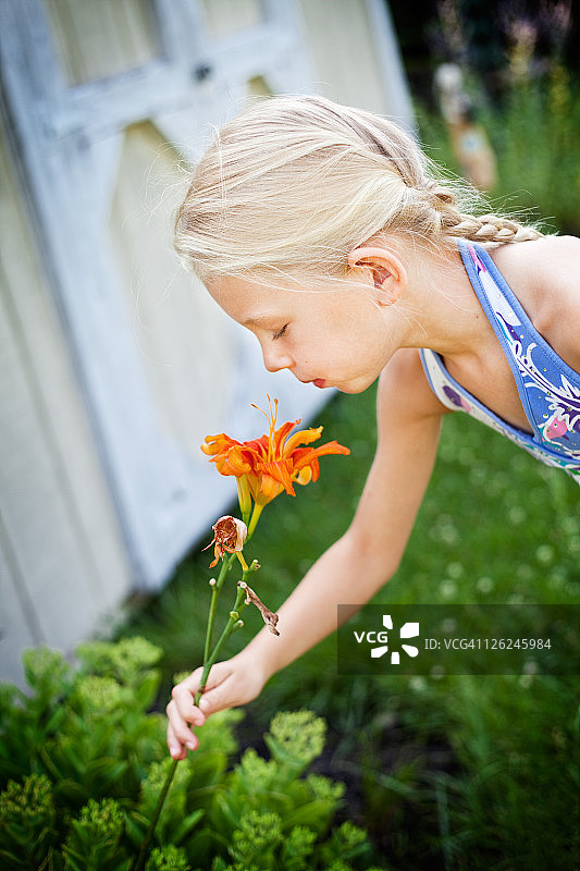 金发女孩嗅着橙色百合花的香味图片素材