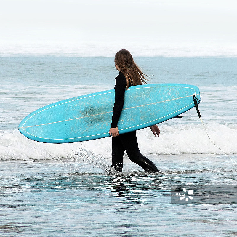 抱着冲浪板在海边行走的女孩图片素材