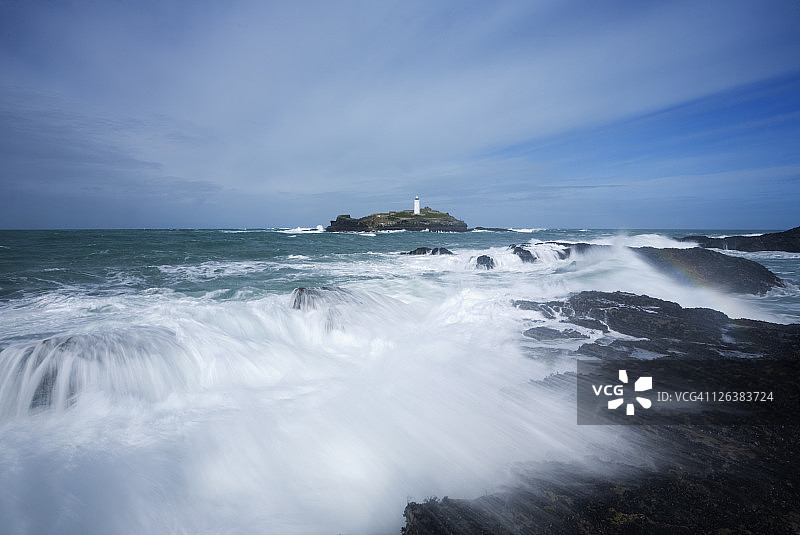 戈德雷维角海浪拍打岩石，远处是戈德雷维灯塔，英国康沃尔图片素材