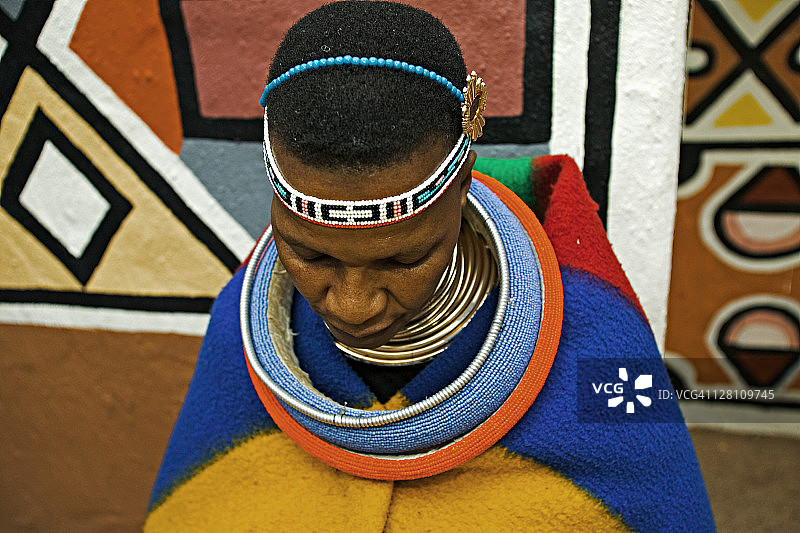 恩德贝勒族妇女身着已婚妇女的传统服装。背景是恩德贝勒村庄的传统几何墙绘，南非约翰内斯堡附近的莱塞迪文化村图片素材