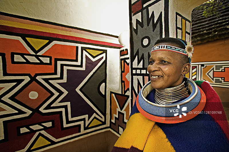 恩德贝勒族妇女身着已婚妇女的传统服装。背景是恩德贝勒村庄的传统几何墙绘，南非约翰内斯堡附近的莱塞迪文化村图片素材