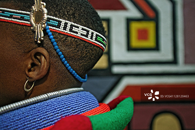 恩德贝勒族妇女身着已婚妇女的传统服装。背景是恩德贝勒村庄的传统几何墙绘，南非约翰内斯堡附近的莱塞迪文化村图片素材