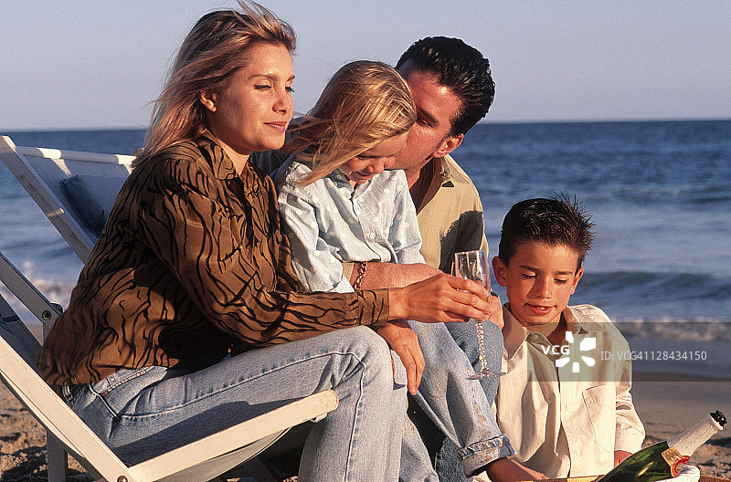 一家人坐在沙滩上，野餐篮里放着香槟图片素材