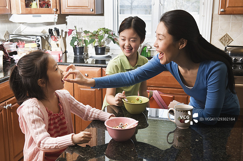 亚洲母亲和女儿在厨房吃早餐。图片素材