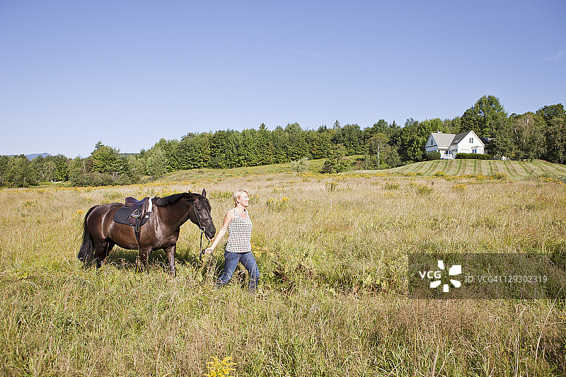 白人女子牵马穿过田野图片素材