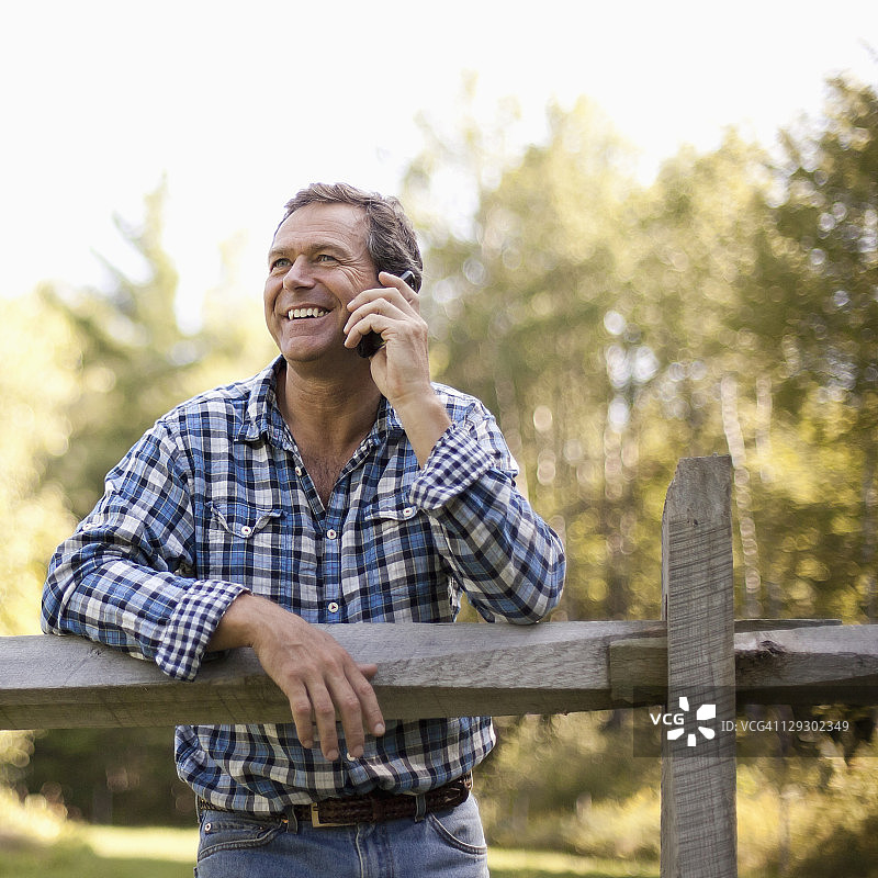 倚靠在栅栏上用手机交谈的白人男子图片素材