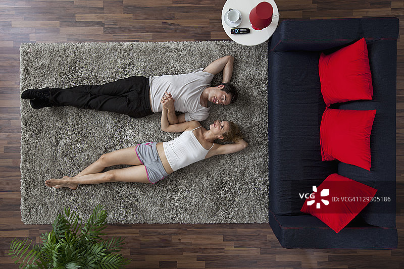 一对夫妇躺在客厅的地毯上，手牵着手，互相凝视（俯视）图片素材