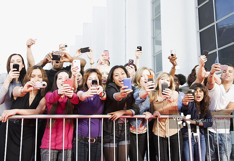 粉丝在屏障后面用手机拍照图片素材
