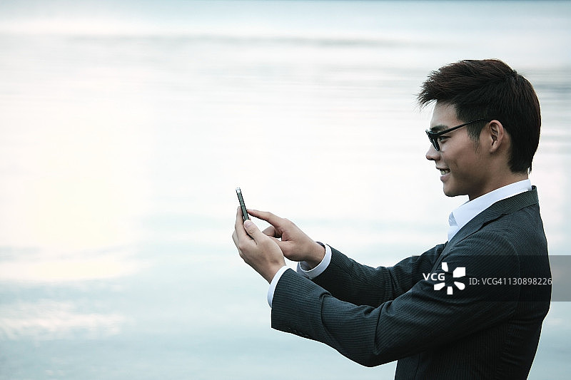 在湖边使用手机的年轻商人图片素材