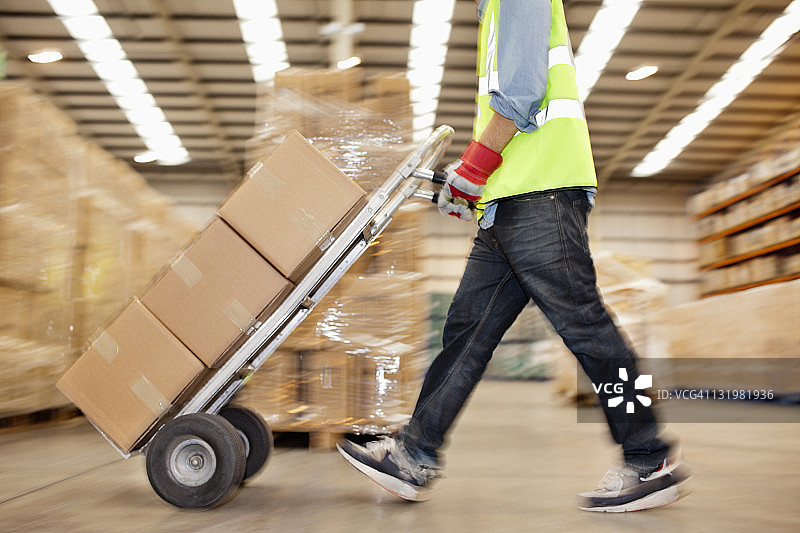工人在仓库里推着装满纸箱的手推车的侧视图图片素材
