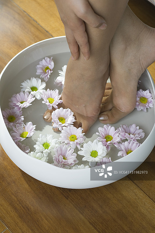 女子将双脚浸泡在装满水和鲜花的碗中图片素材