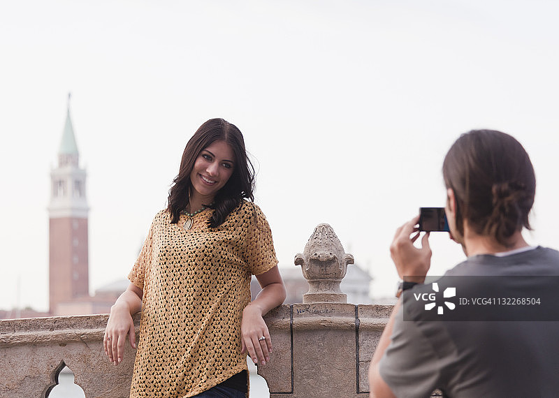 意大利威尼斯：年轻男人在桥上给女人拍照，背景是圣乔治马焦雷教堂图片素材