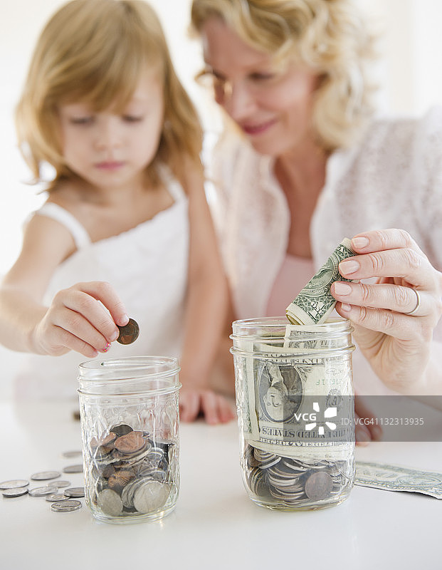 母女一起把钱放进罐子里图片素材