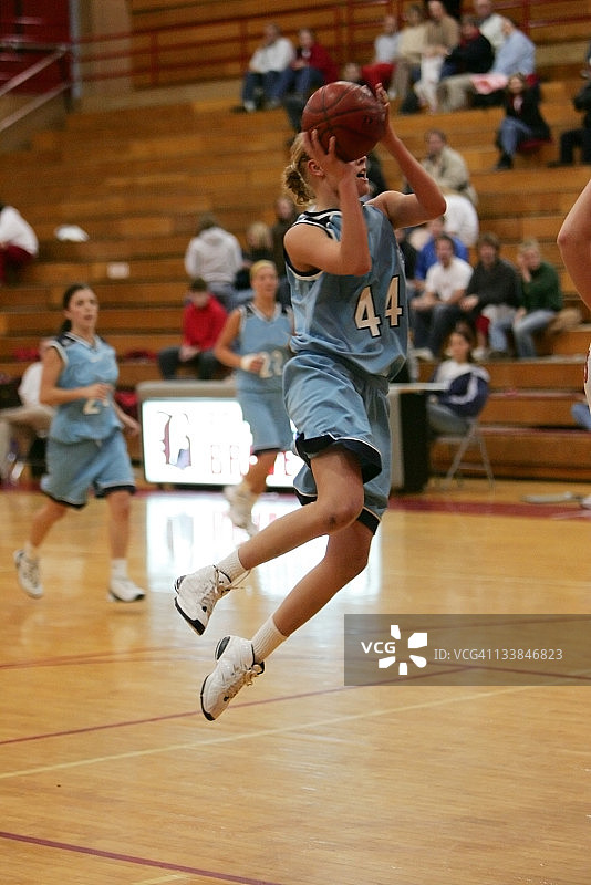 蓝色球衣女子篮球运动员在球场上垂直起跳图片素材