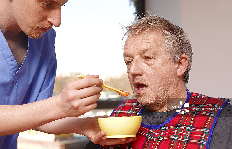 在养老院里，年长的男人被护理员喂食图片素材
