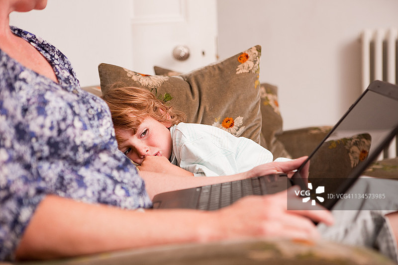 男孩看着母亲使用笔记本电脑图片素材