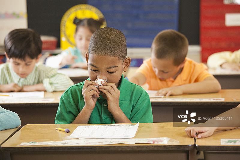 非裔美国学生在教室的课桌旁擦鼻子图片素材