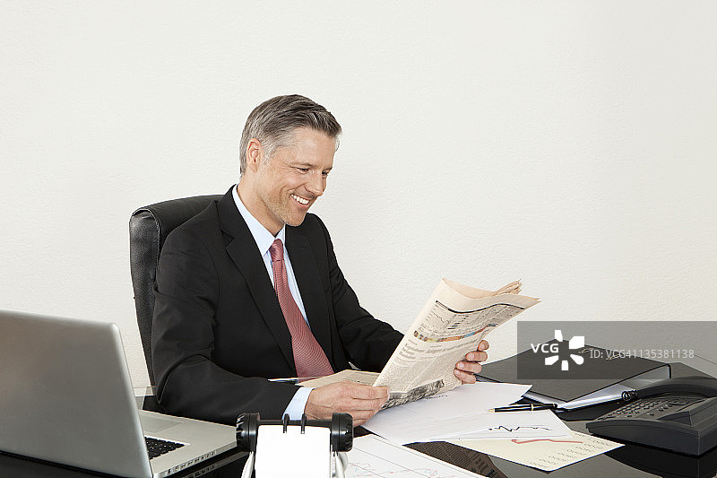 微笑的经理在办公桌前看报纸图片素材